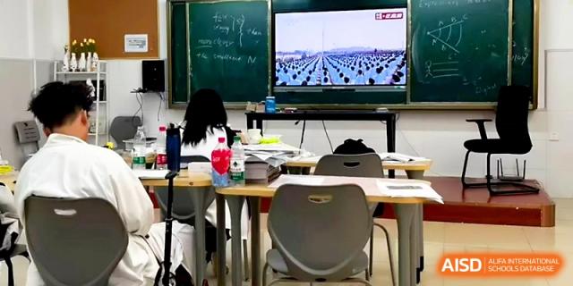 A classroom setup features a digital screen showing a large outdoor assembly, with desks ready for learning at Wuhan Guanggu Future School.
