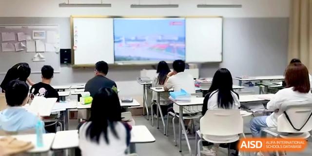 Students sit at their desks in a clean, modern classroom, facing a screen showing a scenic presentation at Wuhan Guanggu Future School.