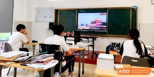 A student sits at a desk filled with books, looking toward a digital screen displaying a historical landmark at Wuhan Guanggu Future School.