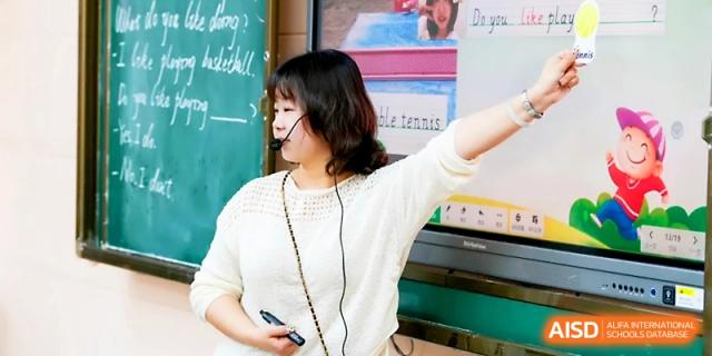 A teacher in a white shirt gestures toward a chalkboard while explaining a concept with a headset microphone at Wuhan Guanggu Future School.