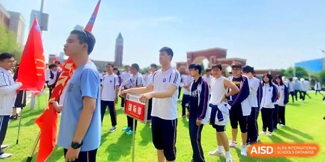 A male student stands in a sports field holding a red sign during an outdoor athletic event at Wuhan Guanggu Future School.