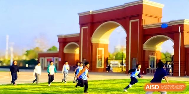Students run through the large, arched red brick gateway of the campus under a clear blue sky at Wuhan Guanggu Future School.