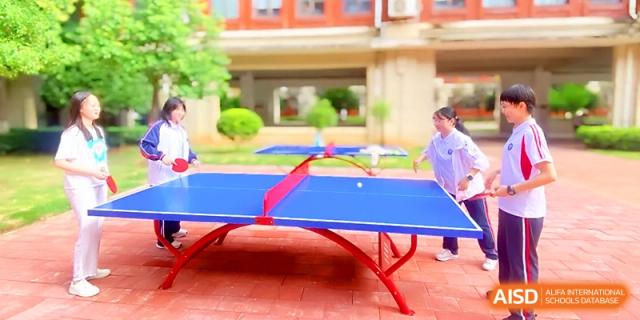 Two students play an energetic game of table tennis on a red outdoor table on the campus grounds at Wuhan Guanggu Future School.
