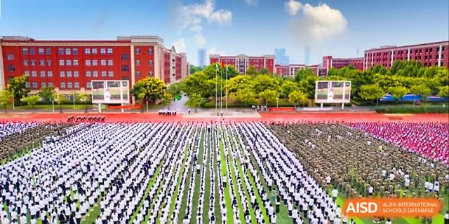 A high-angle view shows thousands of students in uniform standing in perfect rows on a massive field at Wuhan Guanggu Future School.