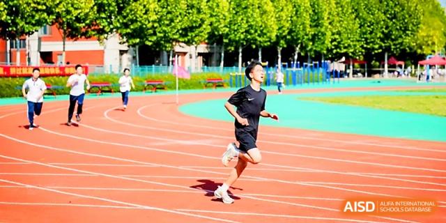 A student in black athletic gear sprints down the orange lanes of the outdoor running track at Wuhan Guanggu Future School.