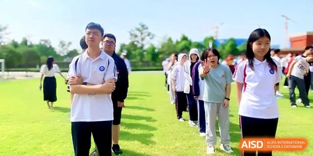 A line of students stands on a grassy field, cheering and gesturing during an outdoor gathering at Wuhan Guanggu Future School.
