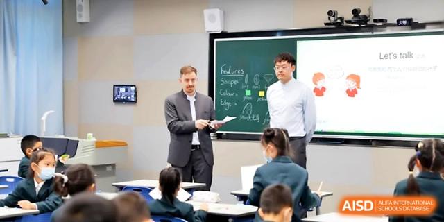Two instructors lead an interactive group discussion with students in a well-equipped, contemporary classroom at Yung Wing School Zhuhai.