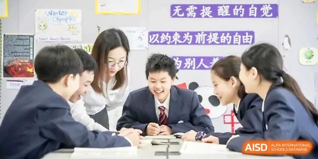 A group of students and their teacher smile while working together on a collaborative tabletop activity at Yung Wing School Zhuhai.