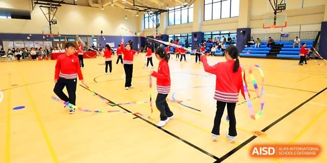 Students in red uniforms participate in a bamboo dance activity in the indoor sports hall at Yung Wing School Zhuhai.