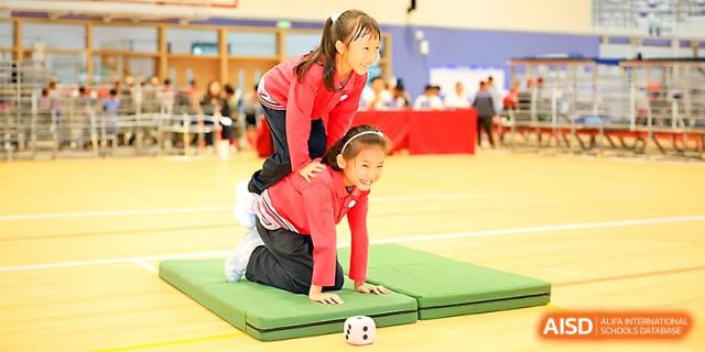 Two students perform a coordinated gymnastic balance move on a green mat during a sports event at Yung Wing School Zhuhai.