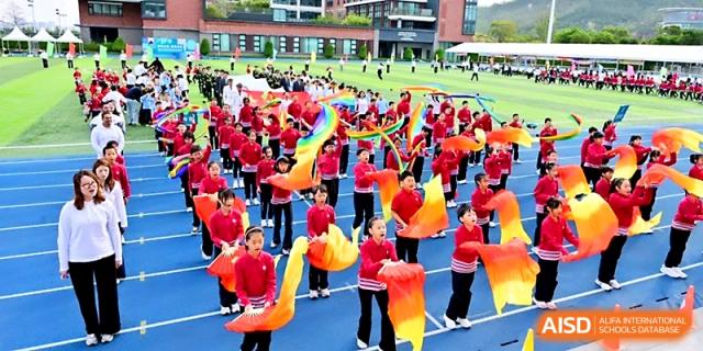 A large group of students performs a synchronized flag dance during an outdoor ceremony at Yung Wing School Zhuhai.