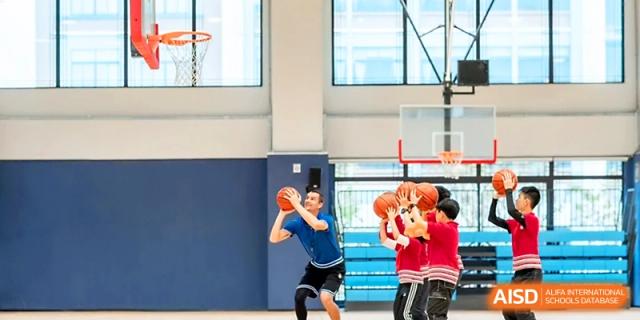 Students practice shooting basketballs under the guidance of a coach in the school gymnasium at Yung Wing School Zhuhai.