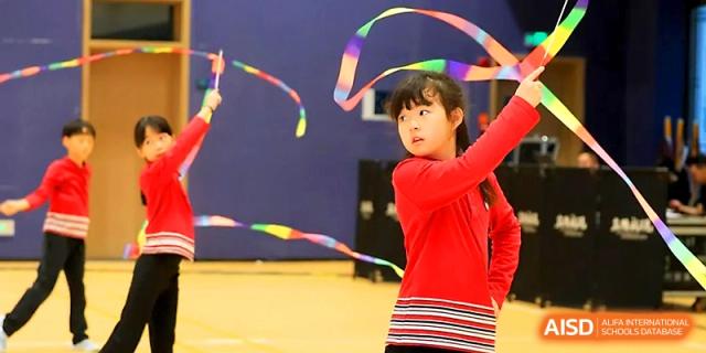 A young girl performs a rhythmic gymnastics routine with a colorful ribbon in the indoor hall at Yung Wing School Zhuhai.
