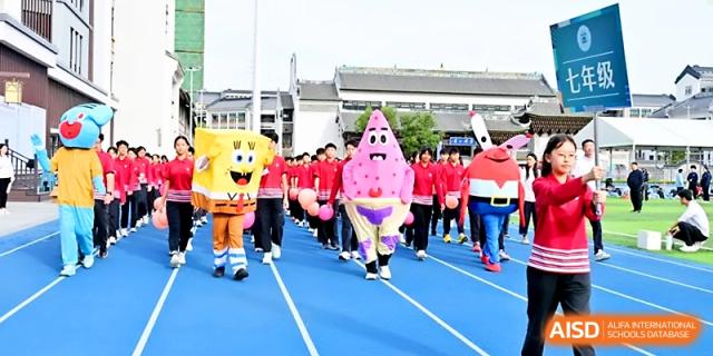 Students parade on the blue athletic track alongside performers in cartoon character mascot suits at Yung Wing School Zhuhai.
