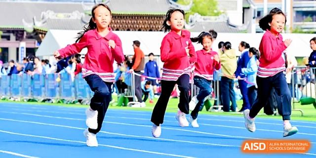 Young girls in red uniforms race down the blue outdoor running track during a track and field meet at Yung Wing School Zhuhai.