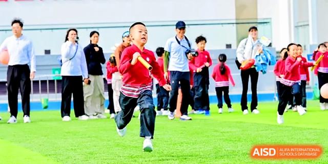 A young boy smiles while participating in a relay race on the green field during sports day at Yung Wing School Zhuhai.