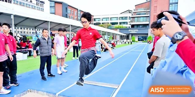 A student athlete performs a long jump over a hurdle on the blue synthetic track at Yung Wing School Zhuhai.