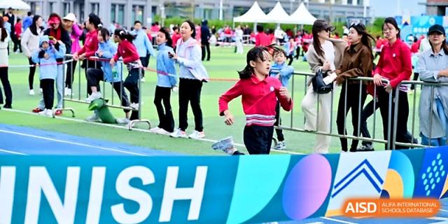 Students compete in a footrace on the outdoor track while spectators cheer from the sidelines at Yung Wing School Zhuhai.