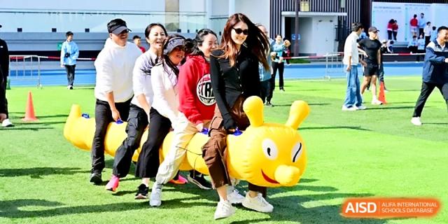 Adults and students participate in a fun team-building activity using a large inflatable yellow caterpillar at Yung Wing School Zhuhai.