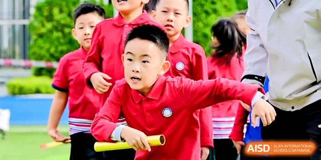 A young boy in a red polo shirt focuses intently on a relay race while holding a baton at Yung Wing School Zhuhai.