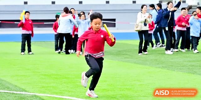 A student in a red shirt and athletic pants runs across a green field during an outdoor sports competition at Yung Wing School Zhuhai.