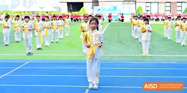 A student in a traditional yellow and white martial arts uniform stands at attention on the athletic track at Yung Wing School Zhuhai.