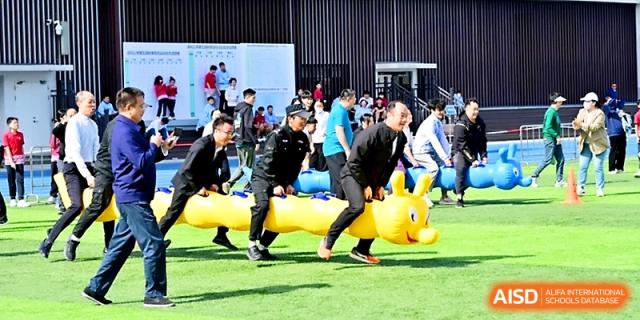 A group of men engages in a competitive and humorous race on an inflatable caterpillar toy during sports day at Yung Wing School Zhuhai.