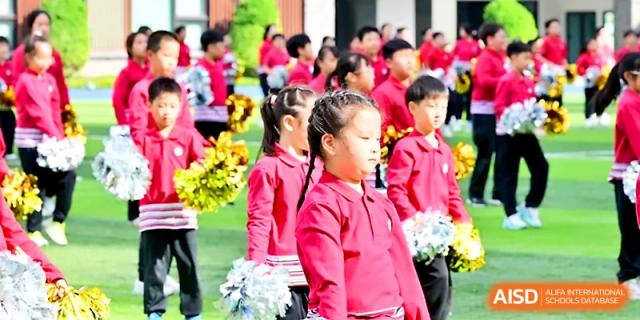 A group of students in red uniforms stands ready with colorful pompoms for a cheerleading performance at Yung Wing School Zhuhai.