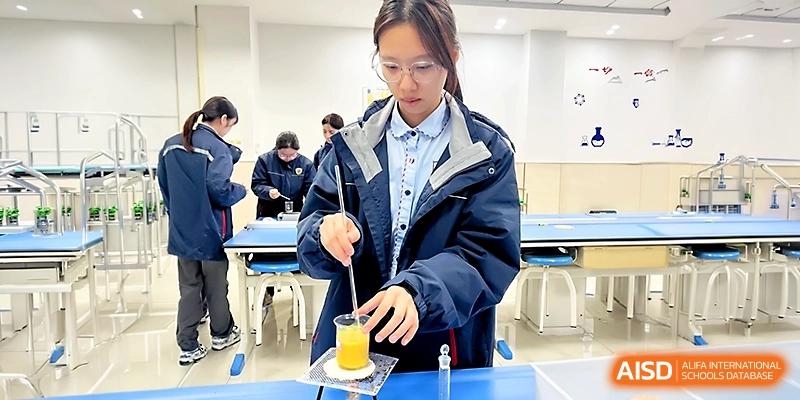 A female student in a lab coat carefully stirs a yellow liquid in a glass beaker during a chemistry experiment at Zhangjiagang Foreign Language School.