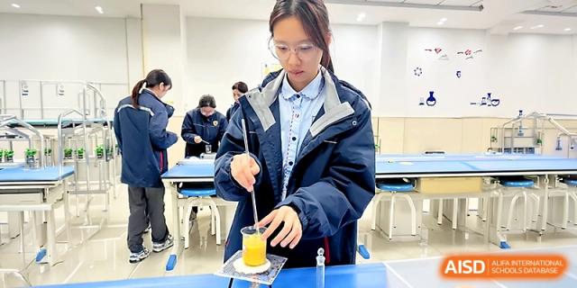 A female student in a lab coat carefully stirs a yellow liquid in a glass beaker during a chemistry experiment at Zhangjiagang Foreign Language School.