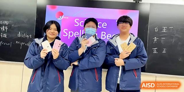 Three students stand proudly in front of a "Science Spelling Bee" screen, holding up their awards and certificates at Zhangjiagang Foreign Language School.
