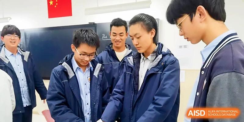 Three male students in blue school jackets stand together, looking down and discussing a shared project or task at Zhangjiagang Foreign Language School.