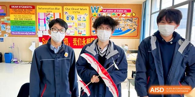Two students pose with a red and white model airplane they constructed, standing in front of a colorful classroom display at Zhangjiagang Foreign Language School.