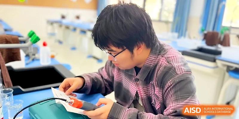 A student in a plaid shirt works intently on a technical project, using tools to assemble an electronic or mechanical device at Zhangjiagang Foreign Language School.