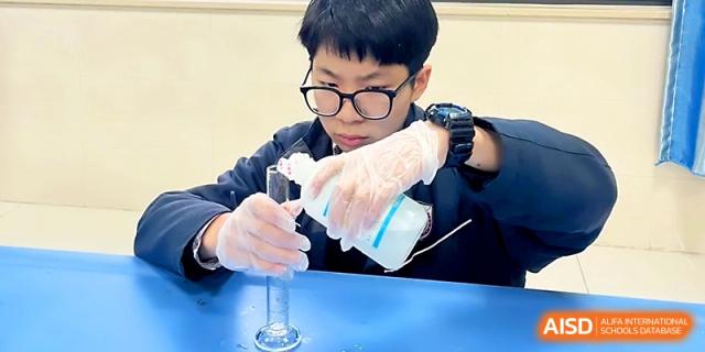 A student wearing gloves carefully pours a liquid into a graduated cylinder during science class at Zhangjiagang Foreign Language School.