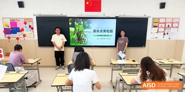 Two presenters stand by a screen displaying a green beverage bottle during a classroom talk at Zhangjiagang Foreign Language School.