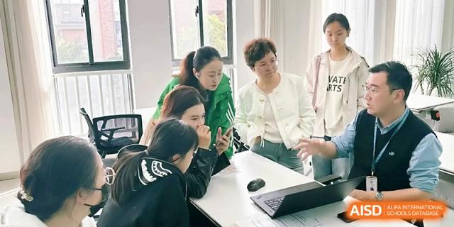 A group of teachers or staff members collaborate around a laptop in a bright office or classroom at Zhangjiagang Foreign Language School.