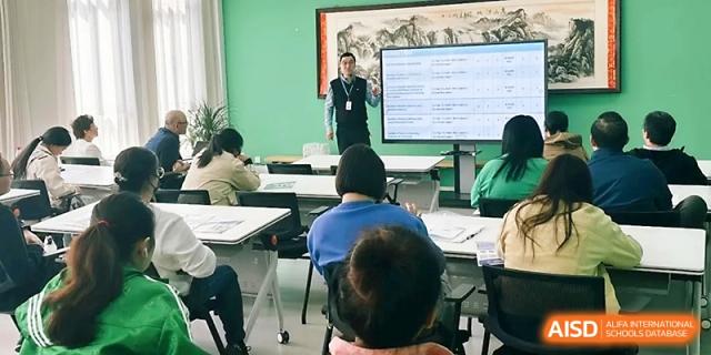 An instructor stands at the front of a classroom, pointing to a screen displaying a digital spreadsheet at Zhangjiagang Foreign Language School.