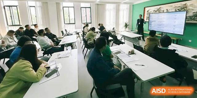 A high-angle view of a professional meeting or workshop taking place in a bright, modern room at Zhangjiagang Foreign Language School.