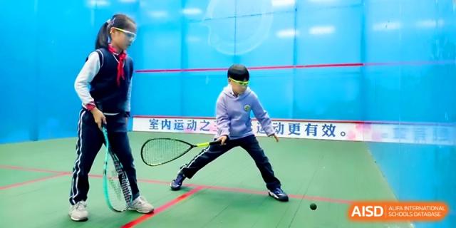 A student in a light blue jacket practices a squash swing on a blue-walled indoor court at Zhangjiagang Foreign Language School.