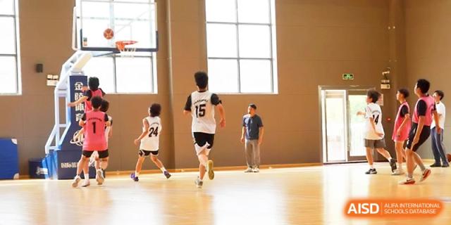 Student basketball players in numbered jerseys run across the court during an indoor game at Zhangjiagang Foreign Language School.