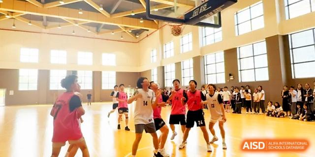 A group of students in red and white jerseys compete in an energetic basketball game in the gym at Zhangjiagang Foreign Language School.