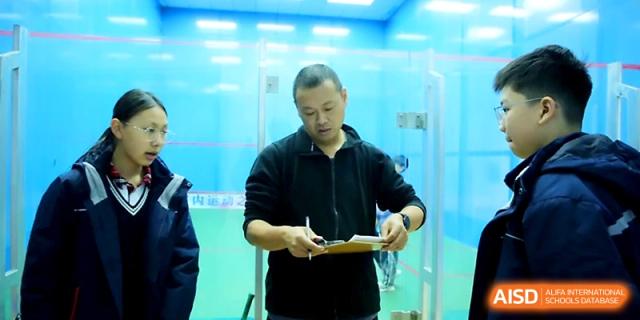 A coach wearing a black jacket reviews a clipboard while standing by an indoor sports court at Zhangjiagang Foreign Language School.