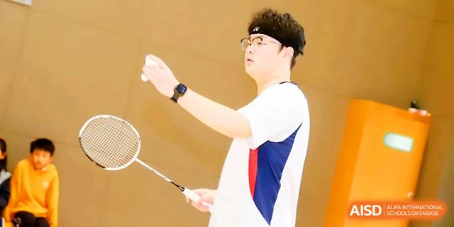 A student in a white sports shirt prepares to serve a shuttlecock during a badminton game at Zhangjiagang Foreign Language School.