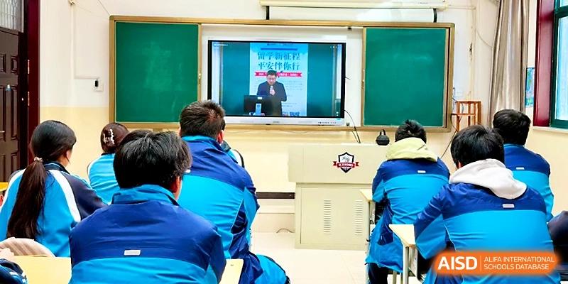 Students in blue uniforms watch an educational video presentation on a large screen at the front of the room at Zhengzhou No.19 High School.