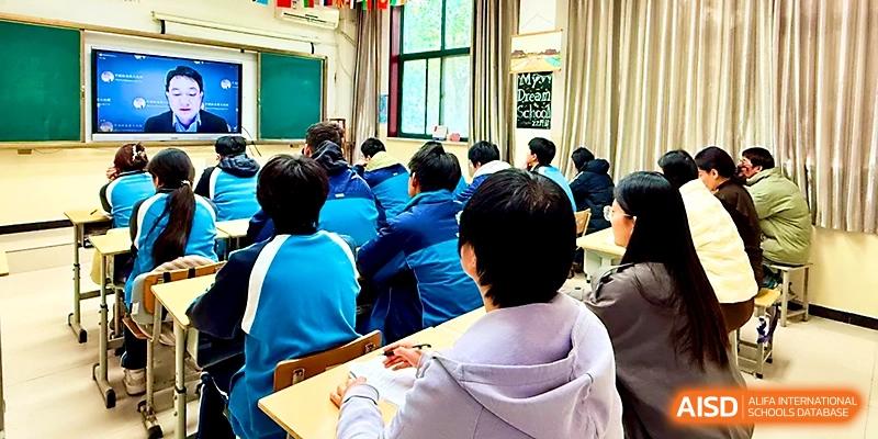 A classroom view from the back shows students in blue jackets looking toward the front during a lesson at Zhengzhou No.19 High School.