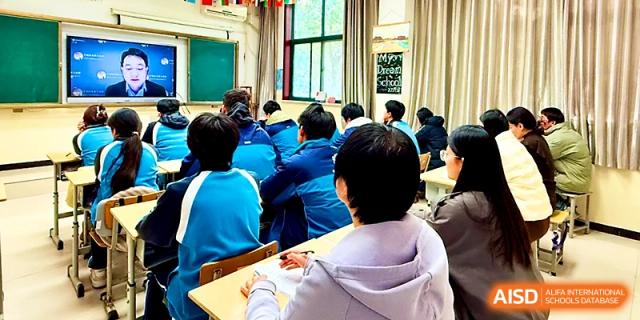 A classroom view from the back shows students in blue jackets looking toward the front during a lesson at Zhengzhou No.19 High School.