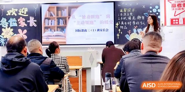 Parents or staff members sit in a classroom attending a presentation shown on a screen at the front at Zhengzhou No.19 High School.