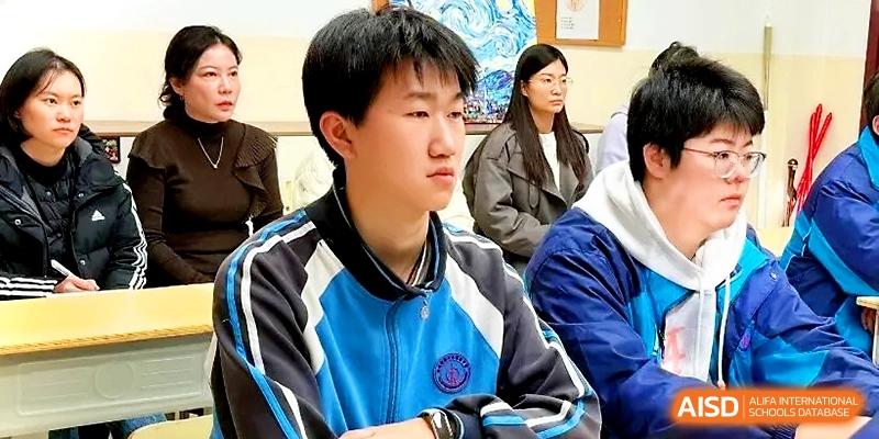 A young male student in a blue athletic uniform looks forward thoughtfully during a classroom discussion at Zhengzhou No.19 High School.