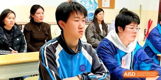 A young male student in a blue athletic uniform looks forward thoughtfully during a classroom discussion at Zhengzhou No.19 High School.